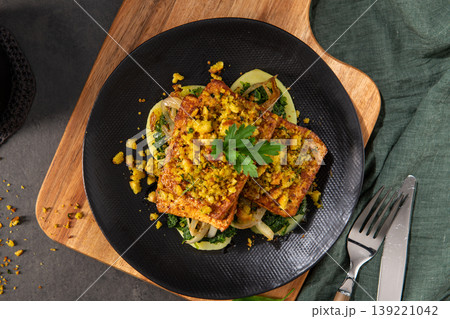 Greens and SlCrusted Tofu Steaks Served with Wilted iced Potatoes on a Black Plate 139221042