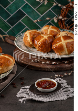 Freshly Baked Hot Cross Buns and Fruit Jam on Rustic Table with Green Tile Backdrop Freshly Baked Hot Cross Buns and Fruit Jam on Rustic Table with Green Tile Backdrop 139221091