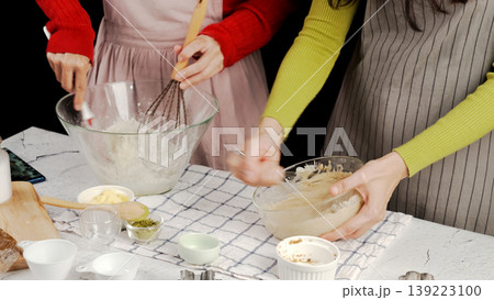 Two people mixing cookie dough together in glass bowls with flour, butter, matcha powder, and tools around them; warm homemade baking moment and collaborative kitchen 139223100