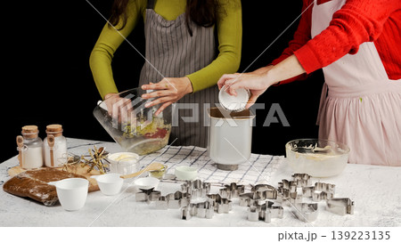 Bakers transferring cookie dough and ingredients into bread maker or dough mixer during recipe video shoot, surrounded by baking tools and cookie cutters 139223135