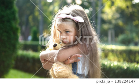 Pretty child girl playing with her favorite teddy bear toy outdoors in summer park. Pretty child girl playing with her favorite teddy bear toy outdoors in summer park. 139224147