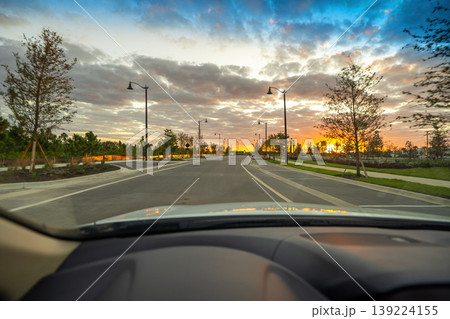 POV driving scene through Florida town during golden hour, dashboard and windshield visible, cars ahead and traffic lights on lively city street. 139224155
