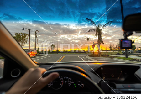 POV commute through rural town district, dashboard visible, cars merging at intersection, street lights turning on as evening approaches. 139224156