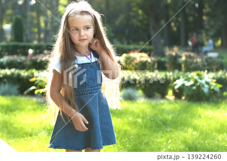 Little pretty child girl with long hair walking outdoors in green summer park on a sunny day. Little pretty child girl with long hair walking outdoors in green summer park on a sunny day. 139224260