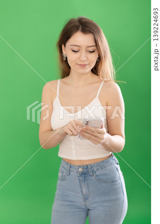 Young woman scrolling smartphone in front of green screen 139224693