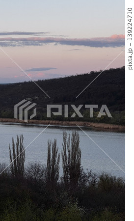 Tranquil river scene featuring trees and gentle hills. 139224710