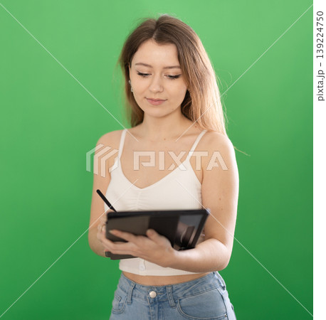 Young woman taking notes on tablet in front of green screen 139224750