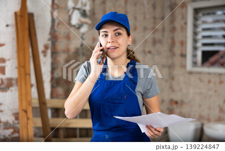 Female foreman holding papers and talking on phone at construction site Female foreman holding papers and talking on phone at construction site 139224847