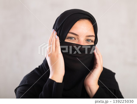 Muslim woman with face covered with burka holds thin fabric of yashmak with her hands Muslim woman with face covered with burka holds thin fabric of yashmak with her hands 139225030