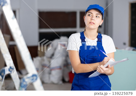 Woman in blue overalls checks the completed construction work on drawing 139225079