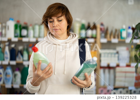 Woman buyer chooses shampoo or shower gel in household goods department of supermarket Woman buyer chooses shampoo or shower gel in household goods department of supermarket 139225328