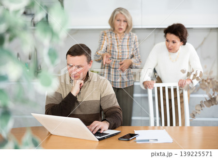 Old and middle-aged woman quarreling angrily to man sitting at the kitchen table Old and middle-aged woman quarreling angrily to man sitting at the kitchen table 139225571