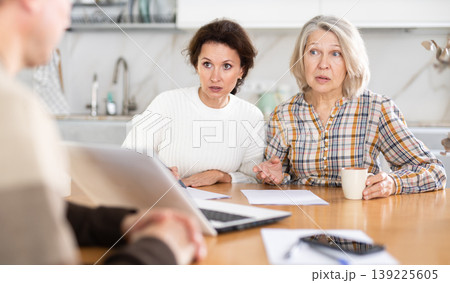 Two women sitting at the kitchen-table face to face with male agent Two women sitting at the kitchen-table face to face with male agent 139225605