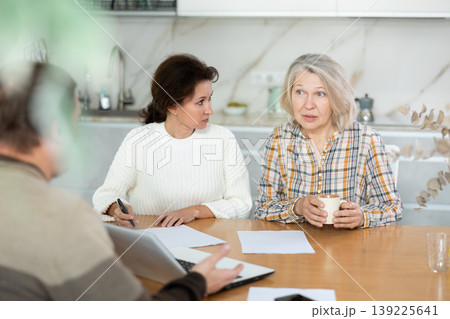 Two women sitting at the kitchen-table face to face with male agent Two women sitting at the kitchen-table face to face with male agent 139225641