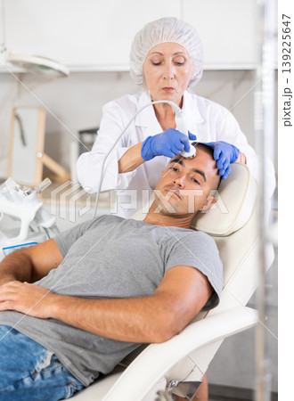 Female cosmetologist performing anti-aging face phototherapy procedure for male client in clinic of aesthetic clinic Female cosmetologist performing anti-aging face phototherapy procedure for male client in clinic of aesthetic clinic 139225647