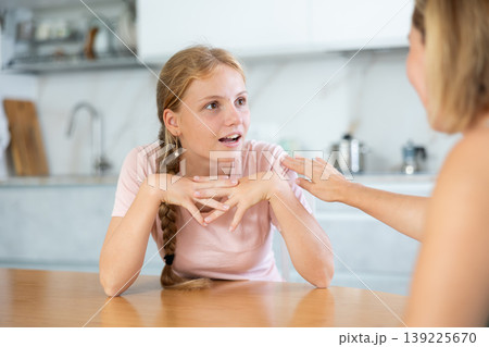 Cheerful teenage girl chatting friendly to mother in home kitchen Cheerful teenage girl chatting friendly to mother in home kitchen 139225670