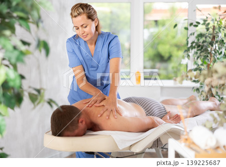 Female masseur performs back stroking and patting during massage session for male client 139225687