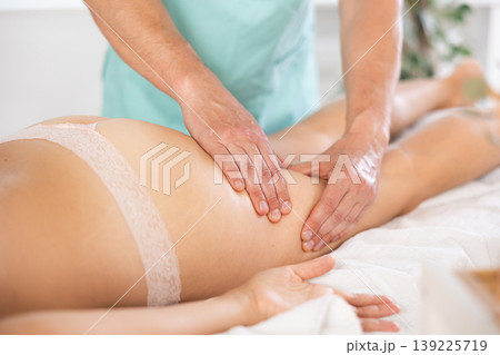 Woman covered with white towel lies and enjoys during anti-cellulite massage in hips and legs 139225719