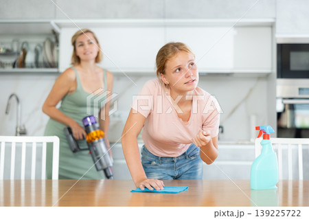 Teen girl help mother and wash dining table in kitchen, blurry mom cleaning using vacuum cleaner Teen girl help mother and wash dining table in kitchen, blurry mom cleaning using vacuum cleaner 139225722
