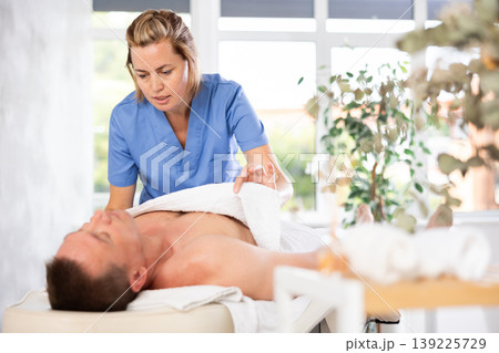 woman covers the man with a towel before massage procedures woman covers the man with a towel before massage procedures 139225729