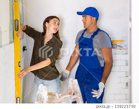 Repairman watching woman measuring wall with spirit level Repairman watching woman measuring wall with spirit level 139225730