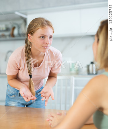 Cheerful teenage girl chatting friendly to mother in home kitchen Cheerful teenage girl chatting friendly to mother in home kitchen 139225785