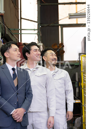 工場で未来を笑顔の横顔で見つめる、見上げるビジネスマンと作業員と3人チームの信頼、信金営業や商工会 工場で未来を笑顔の横顔で見つめる、見上げるビジネスマンと作業員と3人チームの信頼、信金営業や商工会 139226644
