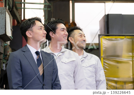 工場で未来を笑顔の横顔で見つめる、見上げるビジネスマンと作業員と3人チームの信頼、信金営業や商工会 工場で未来を笑顔の横顔で見つめる、見上げるビジネスマンと作業員と3人チームの信頼、信金営業や商工会 139226645