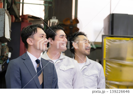 工場で未来を笑顔の横顔で見つめる、見上げるビジネスマンと作業員と3人チームの信頼、信金営業や商工会 工場で未来を笑顔の横顔で見つめる、見上げるビジネスマンと作業員と3人チームの信頼、信金営業や商工会 139226646