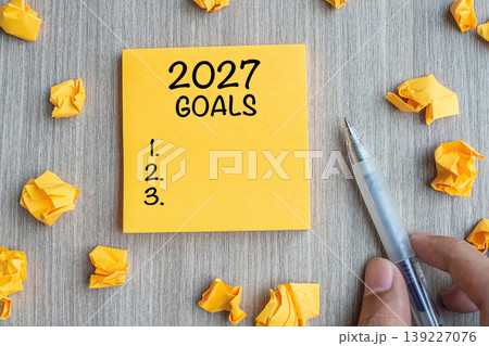 2027 Goal word on yellow note with Businessman holding pen and crumbled paper on wooden table background. New Year New Start, Resolutions, Strategy, mission concept 2027 Goal word on yellow note with Businessman holding pen and crumbled paper on wooden table background. New Year New Start, Resolutions, Strategy, mission concept 139227076