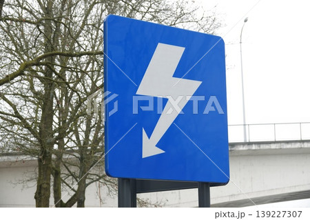 Blue rectangular electric power sign with white lightning bolt at an angle on a pole outdoors 139227307