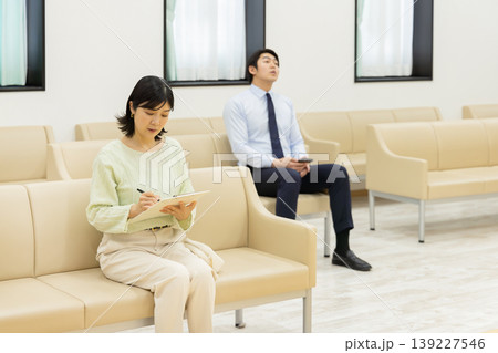 待合室で問診票を記入する女性と順番を待つビジネスマン 待合室で問診票を記入する女性と順番を待つビジネスマン 139227546
