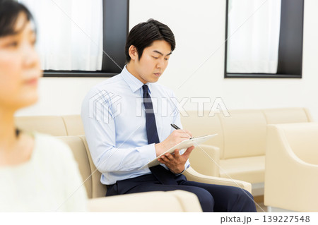 待合室で問診票を記入するビジネスマン 待合室で問診票を記入するビジネスマン 139227548