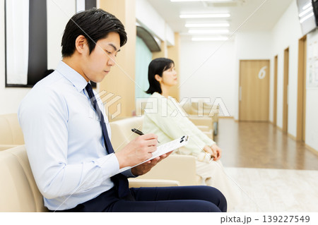 病院の待合室で問診票を記入するビジネスマン 病院の待合室で問診票を記入するビジネスマン 139227549