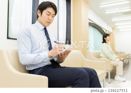 病院の待合室で問診票を記入するビジネスマン 139227551