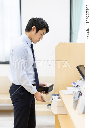 病院の受付で支払いをするビジネスマン 139227560