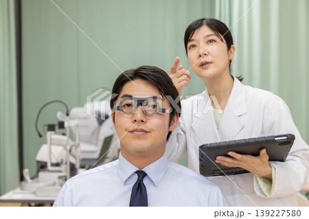 視力検査を受ける男性患者とタブレットで記録する女性医師 視力検査を受ける男性患者とタブレットで記録する女性医師 139227580