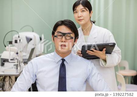 視力検査を受ける男性患者とタブレットで記録する女性医師 139227582
