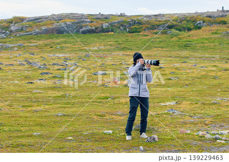 A photographer girl with a professional photo camera walks through a rocky area and on the green meadow in cloudy weather A photographer girl with a professional photo camera walks through a rocky area and on the green meadow in cloudy weather 139229463