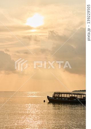 Magical sunset with orange sky at dusk on Maldives islands, silhouette of a tourist boat, the rays of the sun through the clouds, reflection on the water in beach, no people Magical sunset with orange sky at dusk on Maldives islands, silhouette of a tourist boat, the rays of the sun through the clouds, reflection on the water in beach, no people 139229505