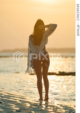 A beautiful tanned girl in a swimsuit stands along a white beach at sunset in the Maldives, she is happy, posing for a photographer A beautiful tanned girl in a swimsuit stands along a white beach at sunset in the Maldives, she is happy, posing for a photographer 139229589