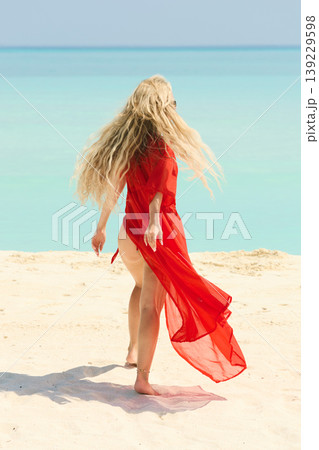 A beautiful tanned girl is wearing in red cape fun on the personal beach of the villa on a sunny day in the Maldives, she is happy and posing A beautiful tanned girl is wearing in red cape fun on the personal beach of the villa on a sunny day in the Maldives, she is happy and posing 139229598