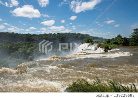 Majestic iguazu falls pouring water creating mist under peaceful blue sky 139229695
