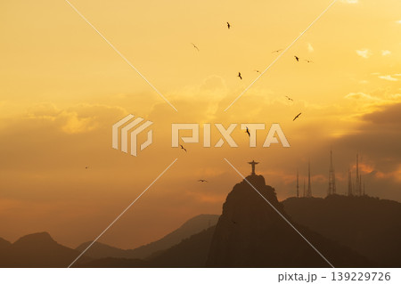 Peaceful sunset over Christ Redeemer statue on mountain in Rio de Janeiro Brazil with birds flying in golden sky Peaceful sunset over Christ Redeemer statue on mountain in Rio de Janeiro Brazil with birds flying in golden sky 139229726