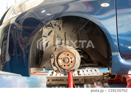 Front car brake disc and wheel hub exposed during maintenance in garage showing automotive repair inspection suspension and safety components on lifted vehicle 139230702
