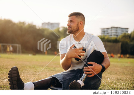 Conception of returning to the sport, sitting. Strong amputee man with prosthesis is with soccer ball on the field 139230828