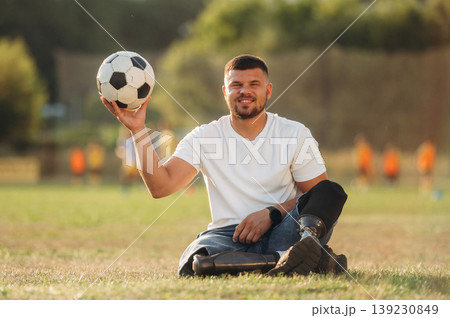 Motivation concept, sitting on the ground. Strong amputee man with prosthesis is with soccer ball on the field 139230849