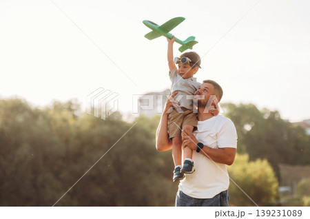 Sitting on the shoulder, holding toy plane. Dad is holding son, having fun on the field Sitting on the shoulder, holding toy plane. Dad is holding son, having fun on the field 139231089