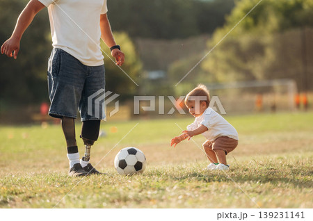 Particle view. Amputee man with prosthesis is playing soccer with his little son on the field Particle view. Amputee man with prosthesis is playing soccer with his little son on the field 139231141