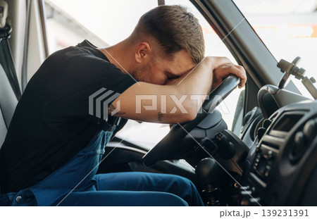 Tired, sleeping on the steering wheel. Inside of the bus with delivery service man in uniform 139231391
